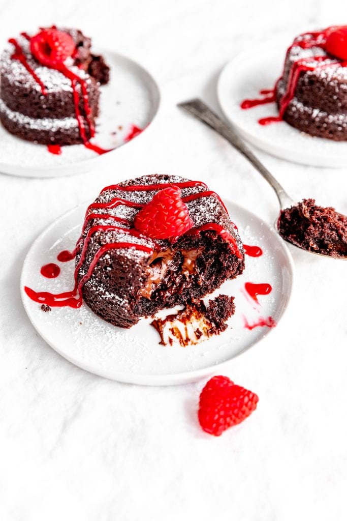 Half of a lava cake oozing chocolate sauce in front of two more plates of cake.