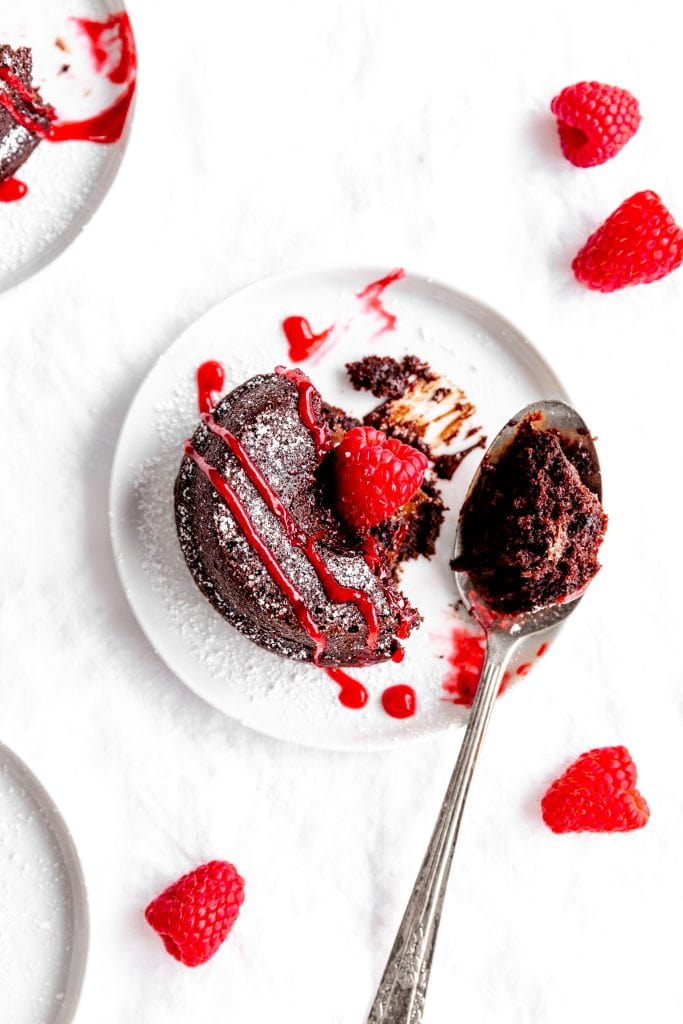 Spoon digging into a lava cake on a white plate.