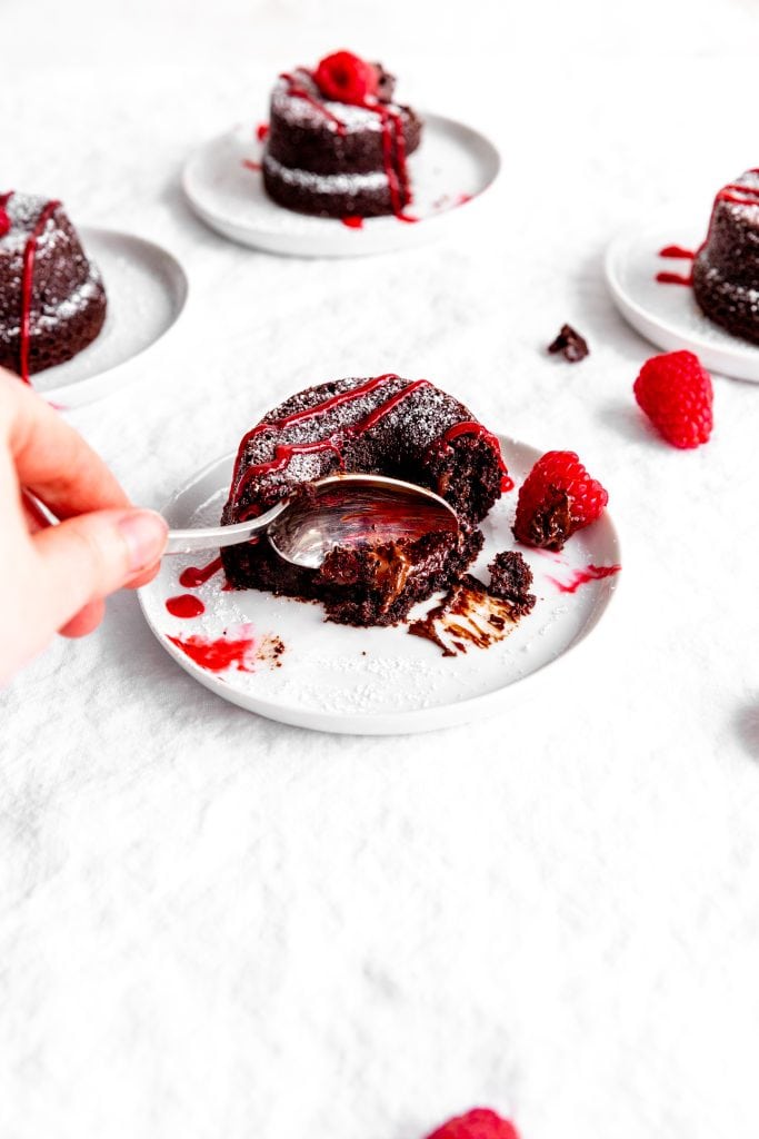 Hand holding a spoon digging into a lava cake drizzled in raspberry sauce.