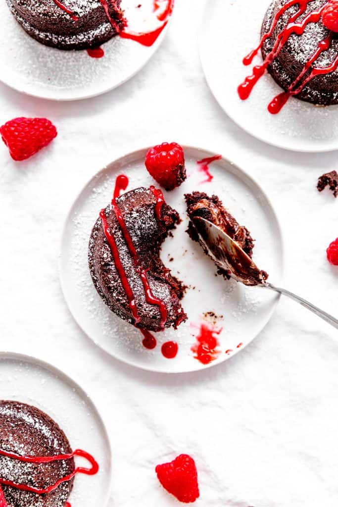 Spoon pulling a bite off of a lava cake on a white plate surrounded by more plates with cakes.