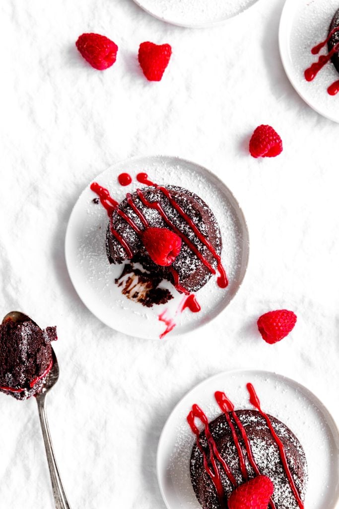 Chocolate lava cake drizzled with raspberry sauce on a white plate next to a spoonful of cake.