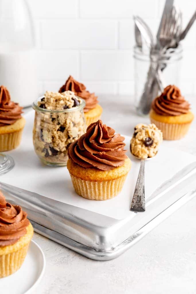 Vegan cookie dough cupcake next to a spoon filled with chocolate chip cookie dough.