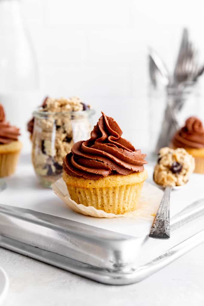 Vegan cookie dough cupcake with its wrapper pulled down next to a spoon filled with cookie dough.