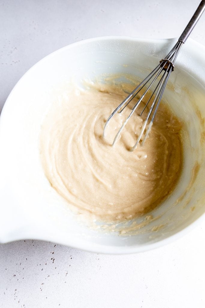 White bowl filled with vanilla cake batter with a whisk.