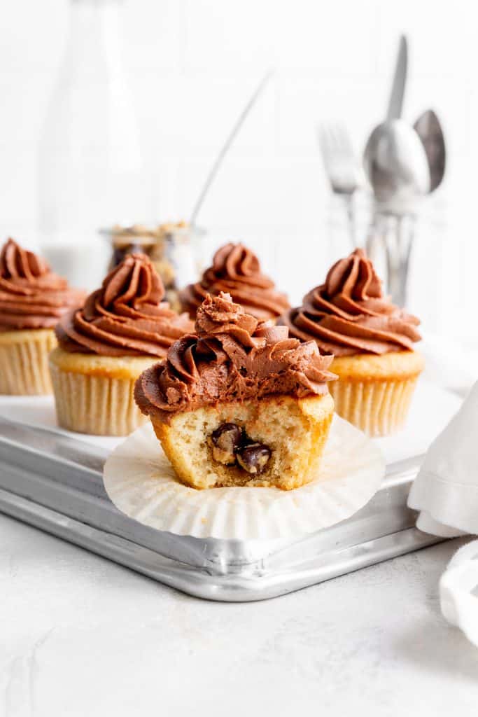 Vegan cookie dough-stuffed cupcake with a bite taken out of it in front of more cupcakes.