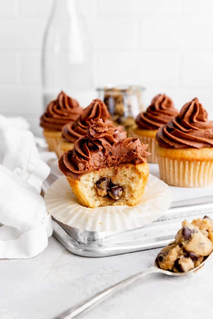 Vegan cookie dough-stuffed cupcake with a bite taken out of it in front of more cupcakes.