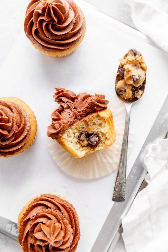 Half of a vegan cookie dough cupcake lying on its side next to a spoon full of chocolate chip cookie dough.