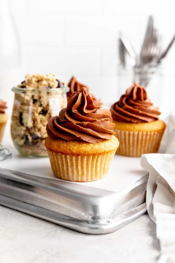 Vegan cookie dough cupcake topped with chocolate frosting in front of a jar of cookie dough.