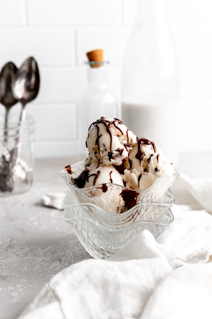 Glass bowl filled with scoops of mint chip ice cream in front of a milk jug.