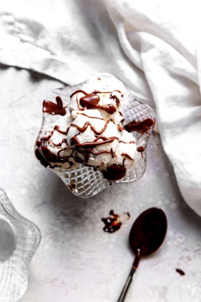 Glass bowl filled with mint chip ice cream drizzled with hot fudge and a white linen napkin.