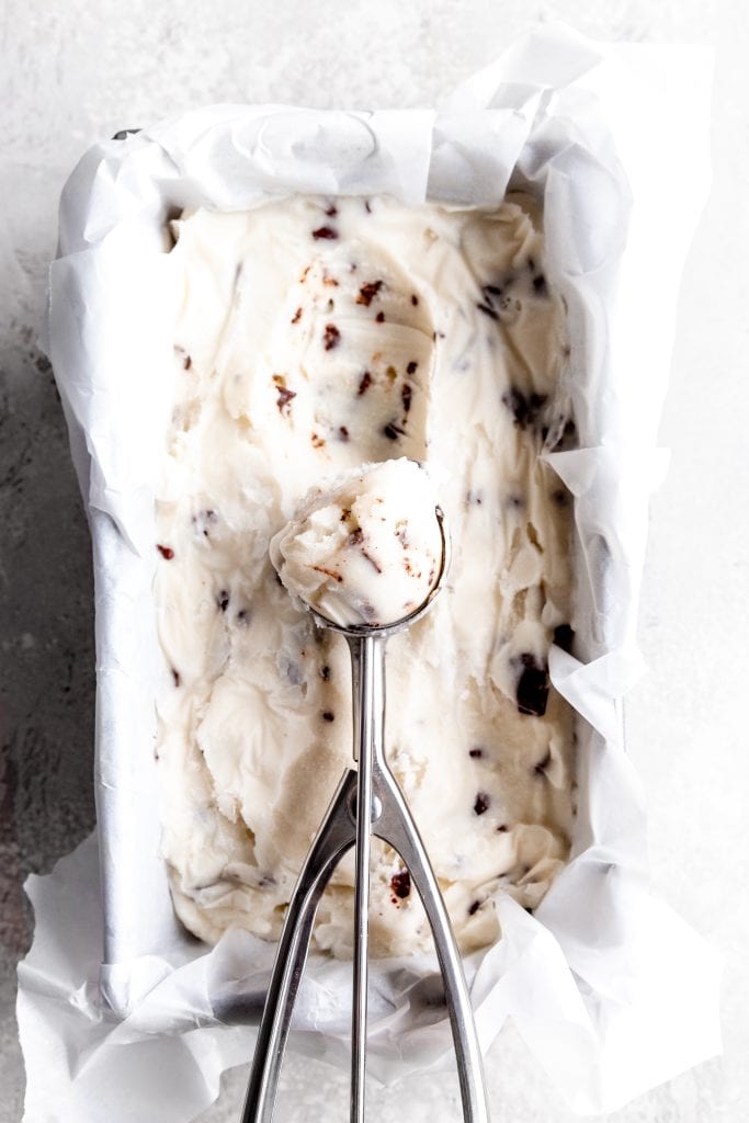 Silver ice cream scoop full of mint chip ice cream in a loaf pan filled with ice cream.