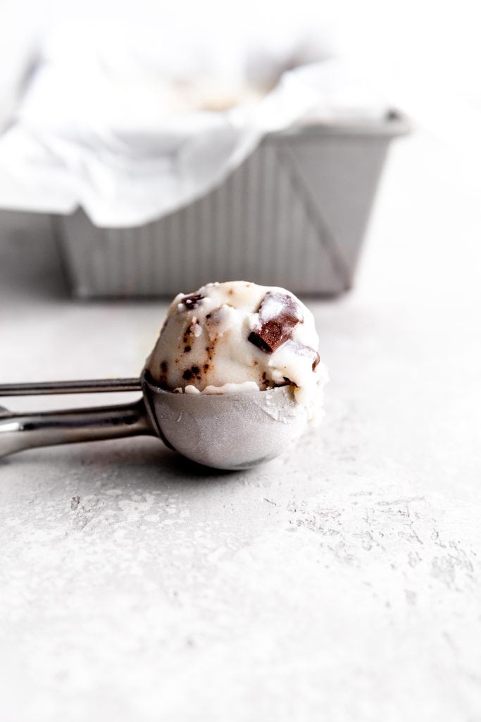 Ice cream scoop filled with mint chip ice cream lying on its side in front of a pan of ice cream.