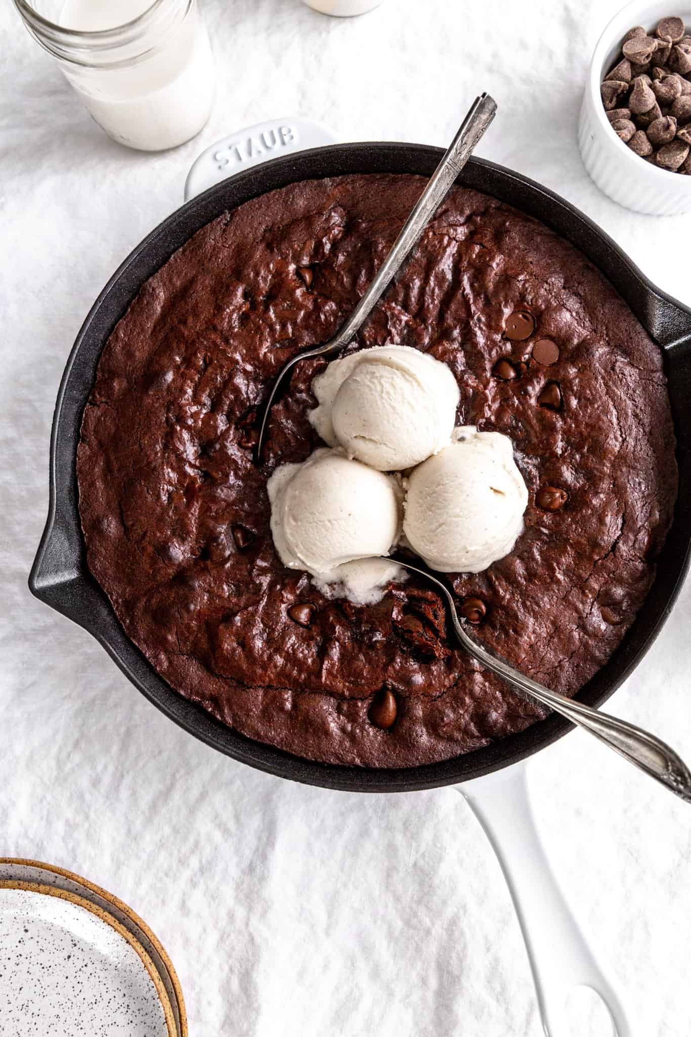 Multiple spoons digging into a vegan skillet brownie topped with vanilla ice cream.