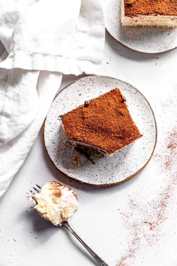 Slice of vegan tiramisu on a white plate with a bite missing.