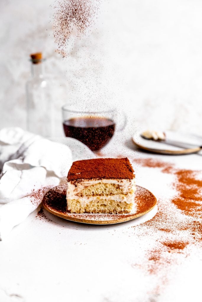 Cocoa powder being dusted onto a slice of vegan tiramisu.