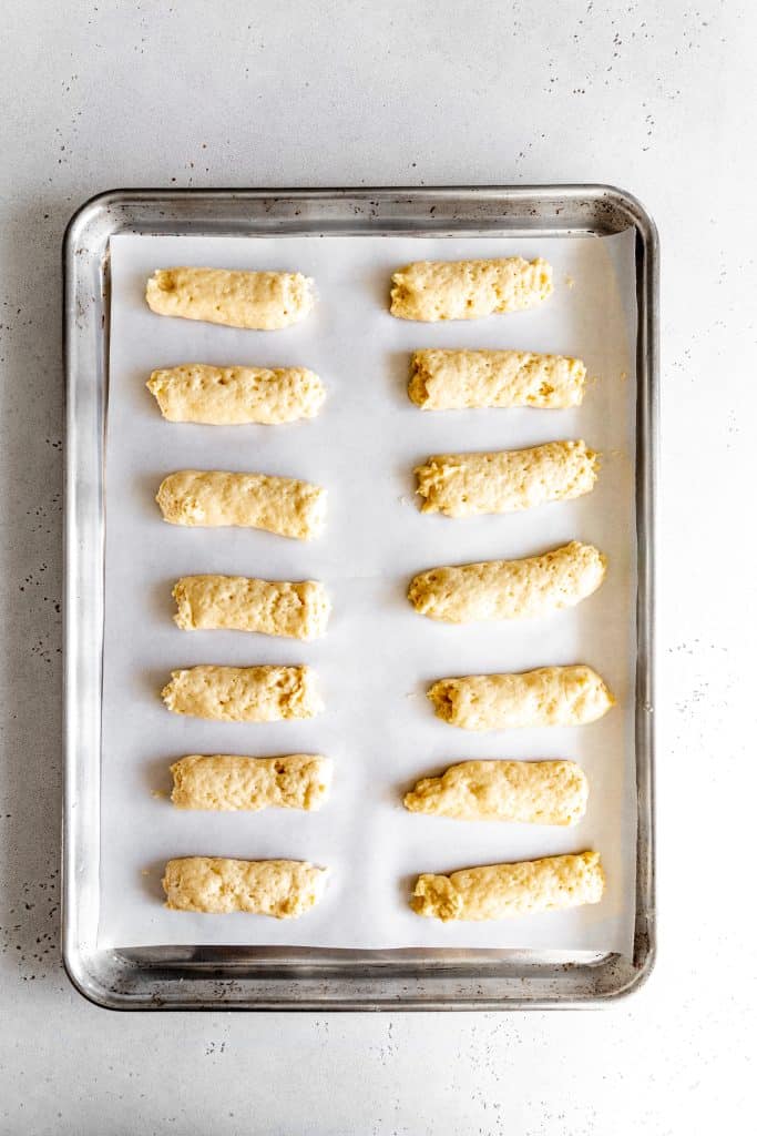 Unbaked ladyfingers on a baking sheet lined with parchment paper.