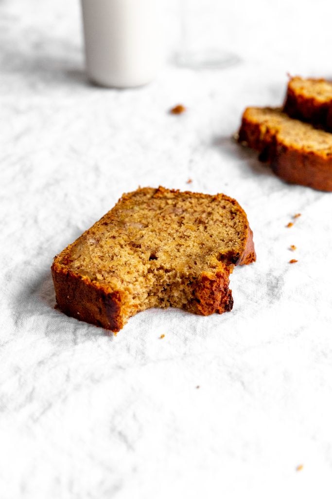 Slice of vegan banana bread with a bite taken out of it in front of jug of milk.