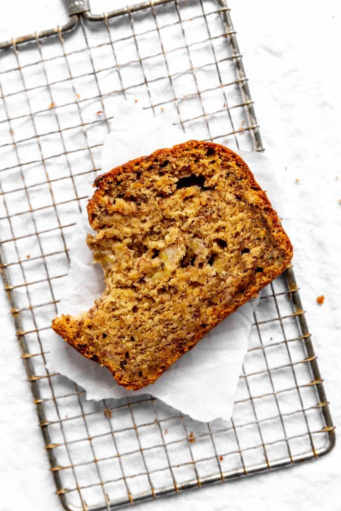 Slice of banana bread with a bite taken out of it on a wire cooling rack.