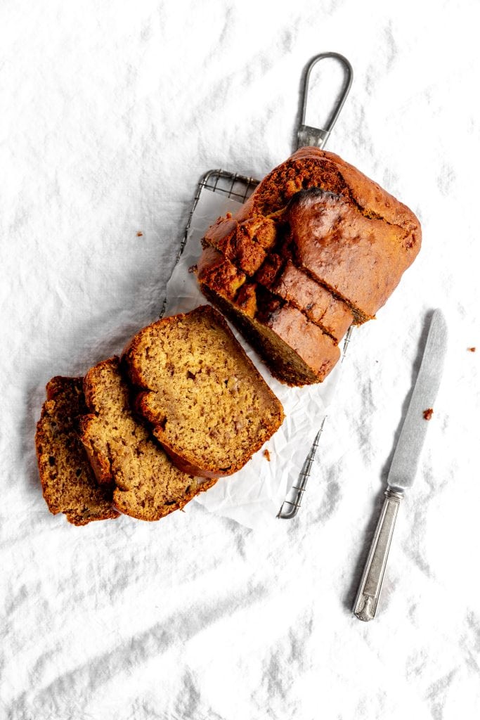 Sliced loaf of vegan banana bread on a wire cooling rack and a knife.