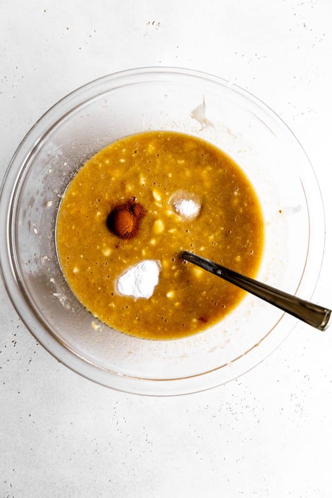 Mashed banana in a glass bowl with spices sprinkled on top.