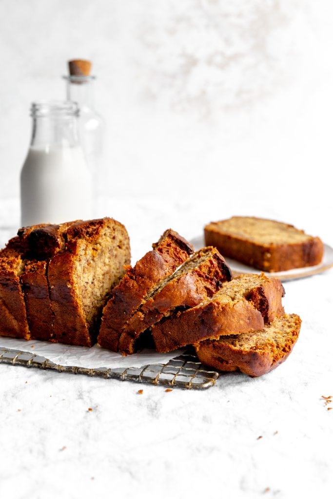 Sliced vegan banana bread on a cooling tack in front of a jug of milk.