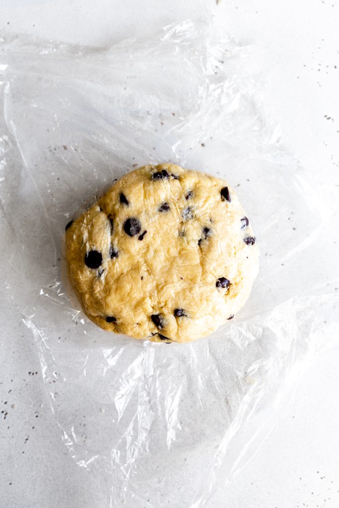 Disk of chocolate chip scone dough sat on a sheet of plastic wrap.