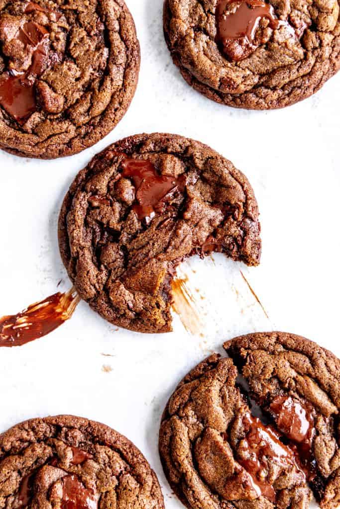 Double chocolate cookie with a bite taken out of it surrounded by more cookies on a baking sheet.