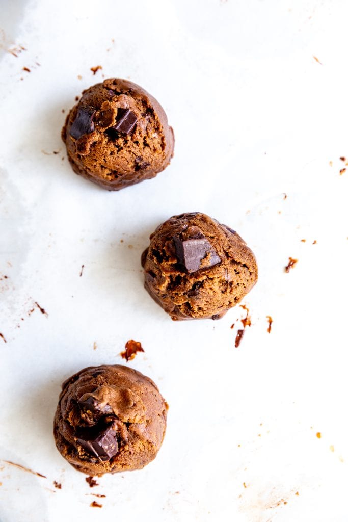 Three unbaked vegan double chocolate cookies on a baking sheet.