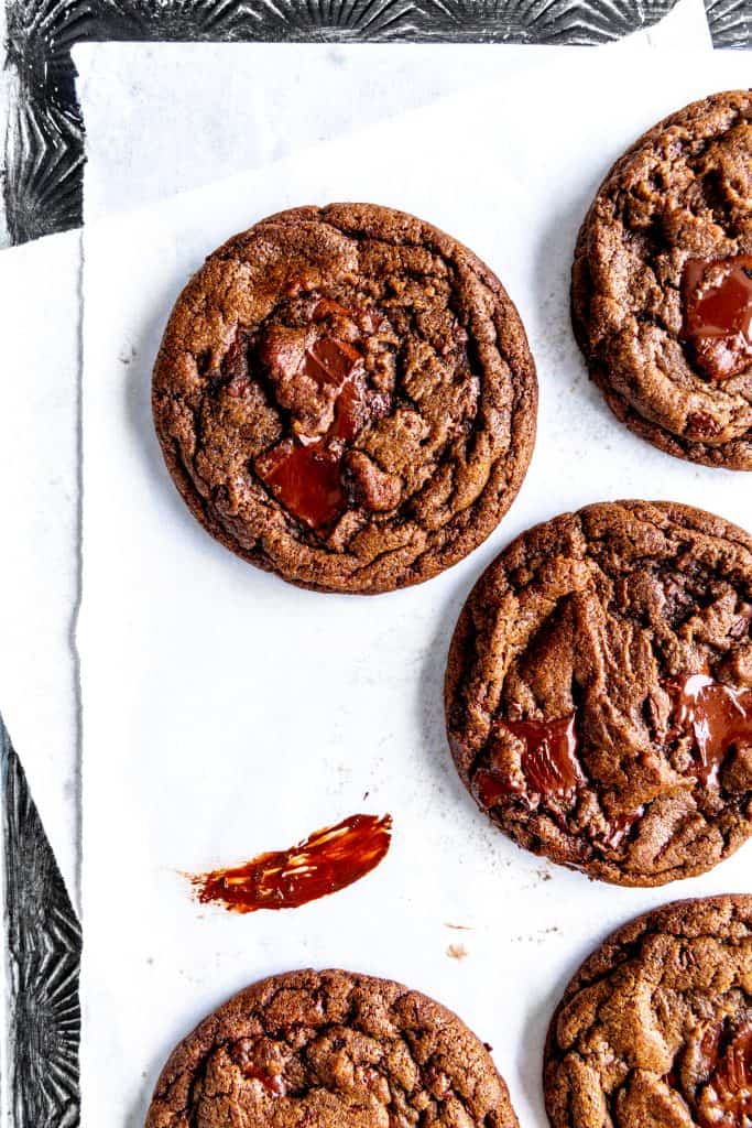 Double chocolate cookies on layered parchment paper smeared with chocolate.