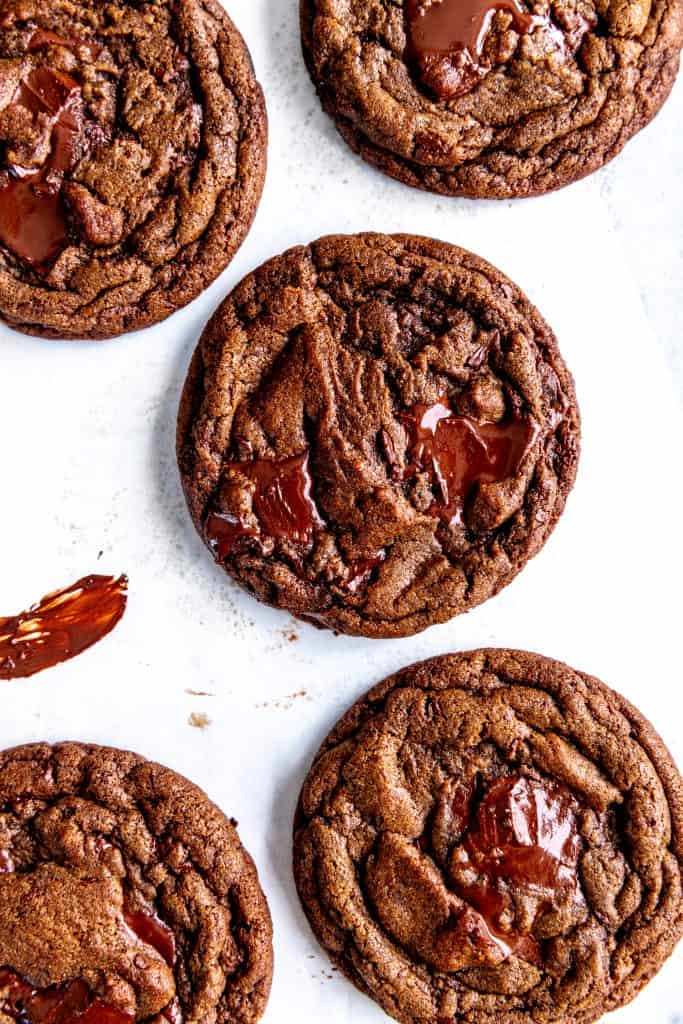 Double chocolate cookies on layered parchment paper smeared with chocolate.