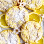 Lemon crinkle cookies on a baking sheet with lemon slices and flowers.