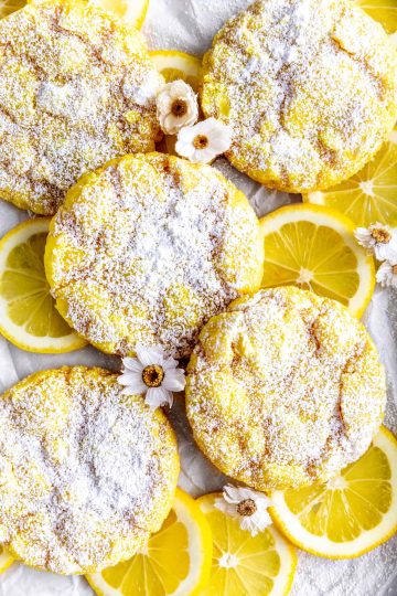 Lemon crinkle cookies on a baking sheet with lemon slices and flowers.