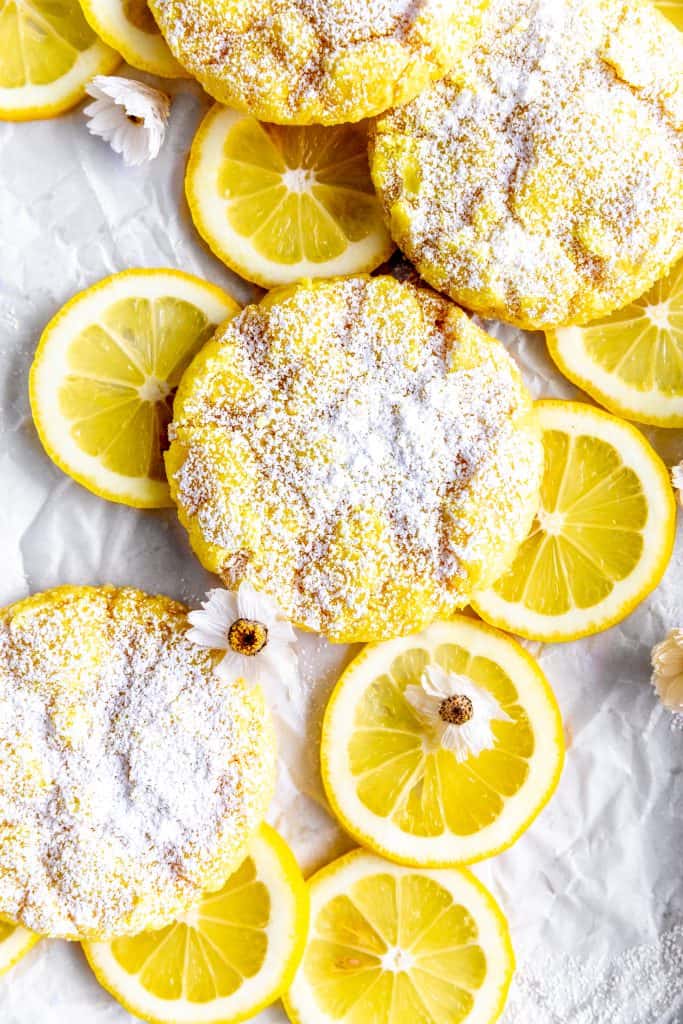 Lemon crinkle cookies on a baking sheet with lemon slices and flowers.