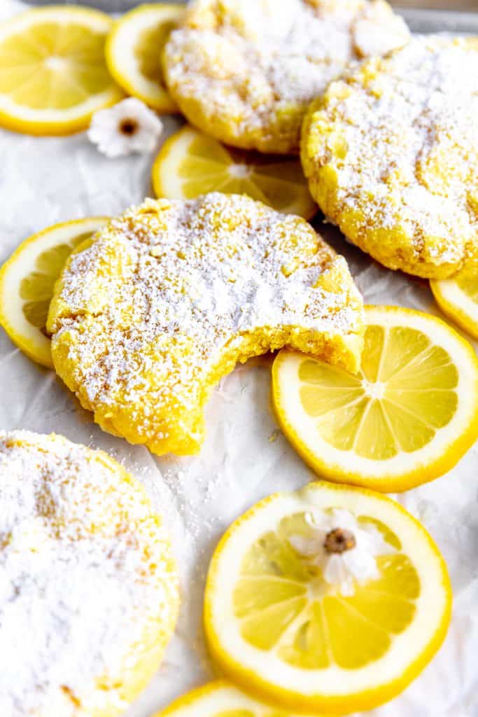 Lemon crinkle cookie with a bite taken out of it, lemon slices and flowers.