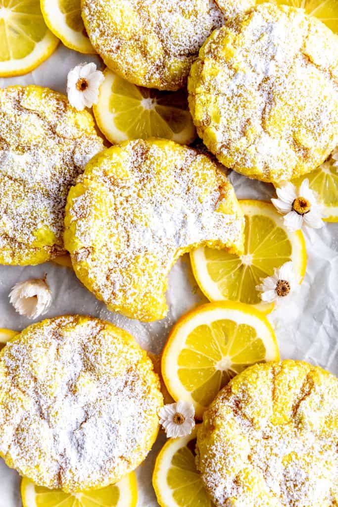 Lemon crinkle cookie with a bite taken out of it, lemon slices and flowers.