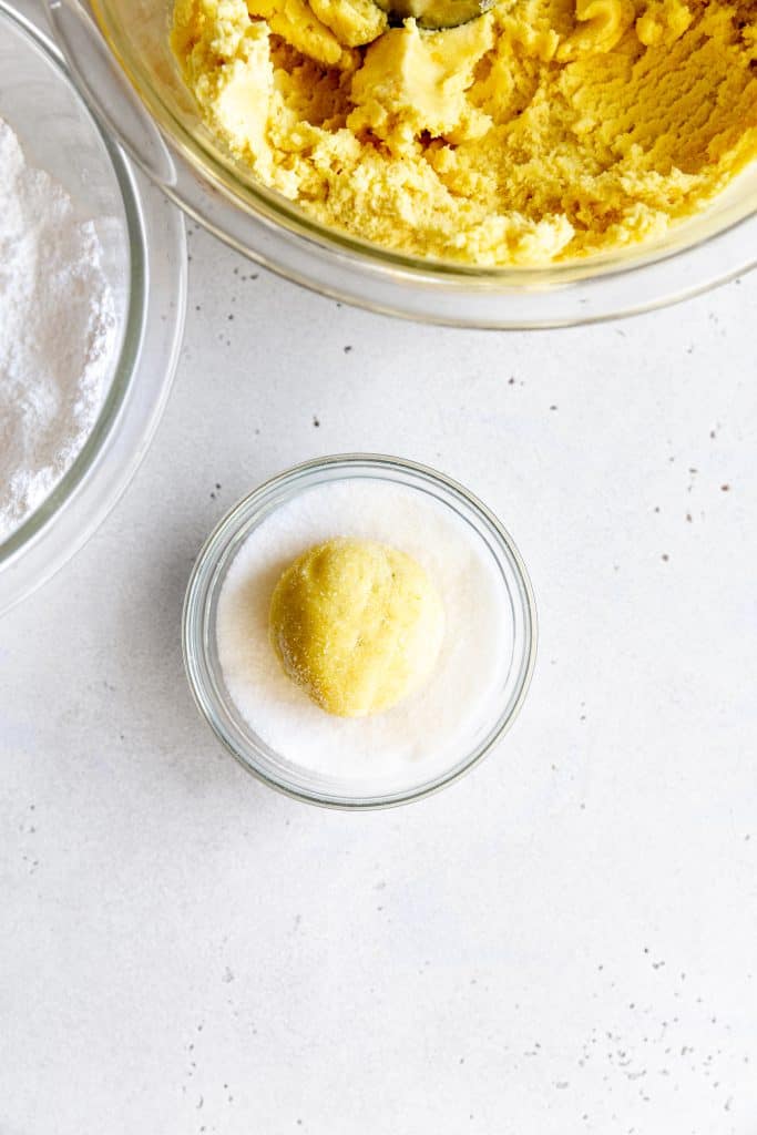 Ball of lemon cookie dough in a glass bowl of granulated sugar.