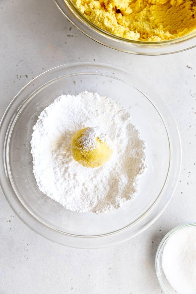 Ball of lemon cookie dough in a glass bowl of powdered sugar.