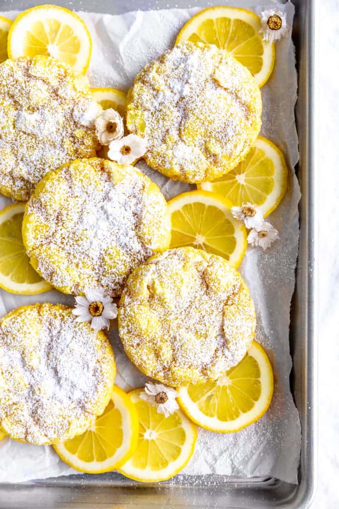 Lemon crinkle cookies on a baking sheet with lemon slices and flowers.