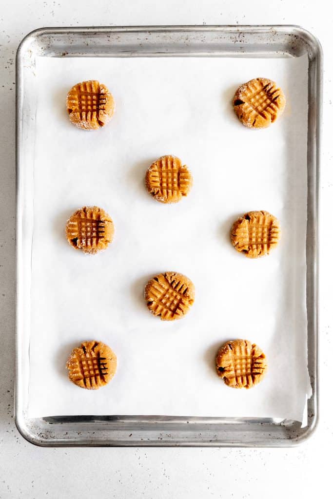 Unbaked peanut butter cookies on a baking sheet lined with parchment.