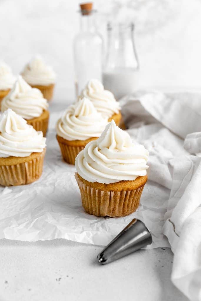 Vanilla cupcakes on a white surface and a jug of milk.