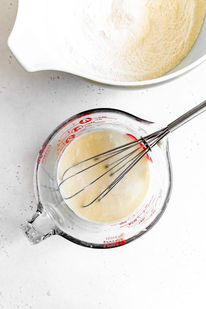 Glass measuring cup of milk and a whisk.