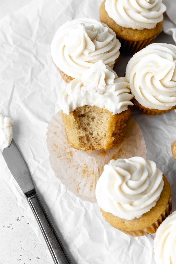 Vanilla cupcake with a bite taken out of it propped against more cupcakes.