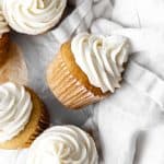 Vanilla cupcake with vanilla icing on its side on a linen napkin.