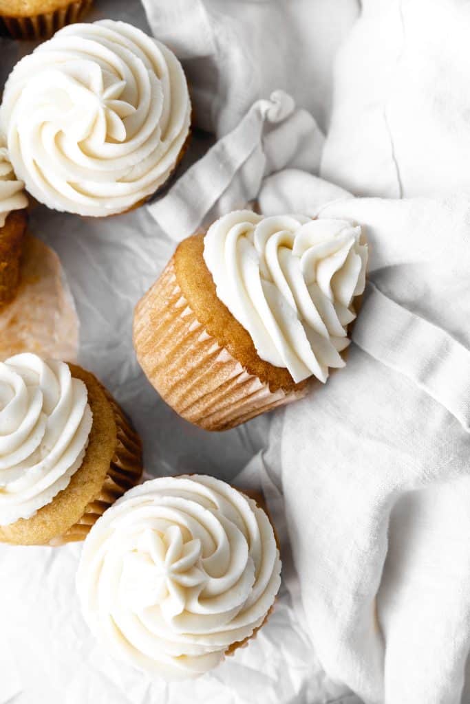 Vanilla cupcake with vanilla icing on its side on a linen napkin.