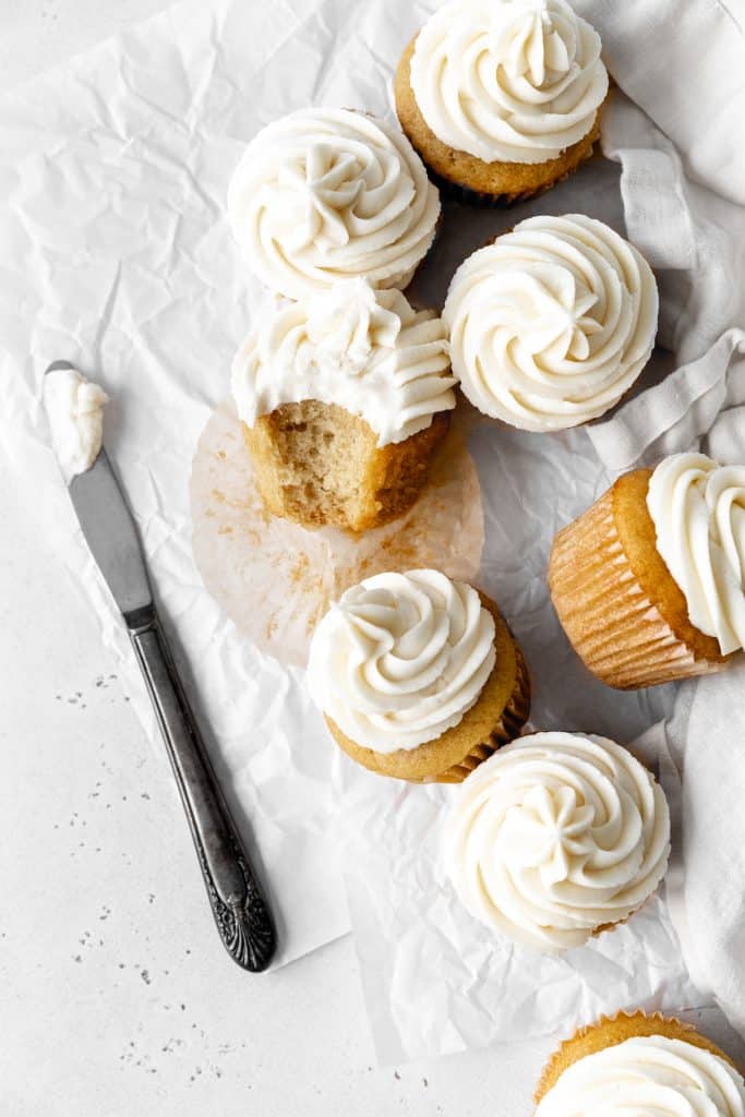 Vanilla cupcake with a bite taken out of it propped against more cupcakes.