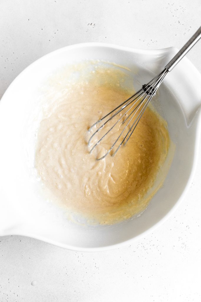 White bowl filled with vanilla cake batter and a whisk.