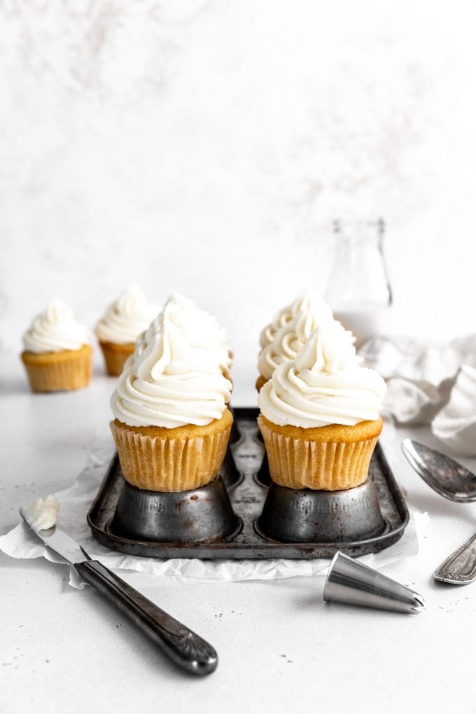 Vanilla cupcakes on a cupcake pan in front of a jug of milk.