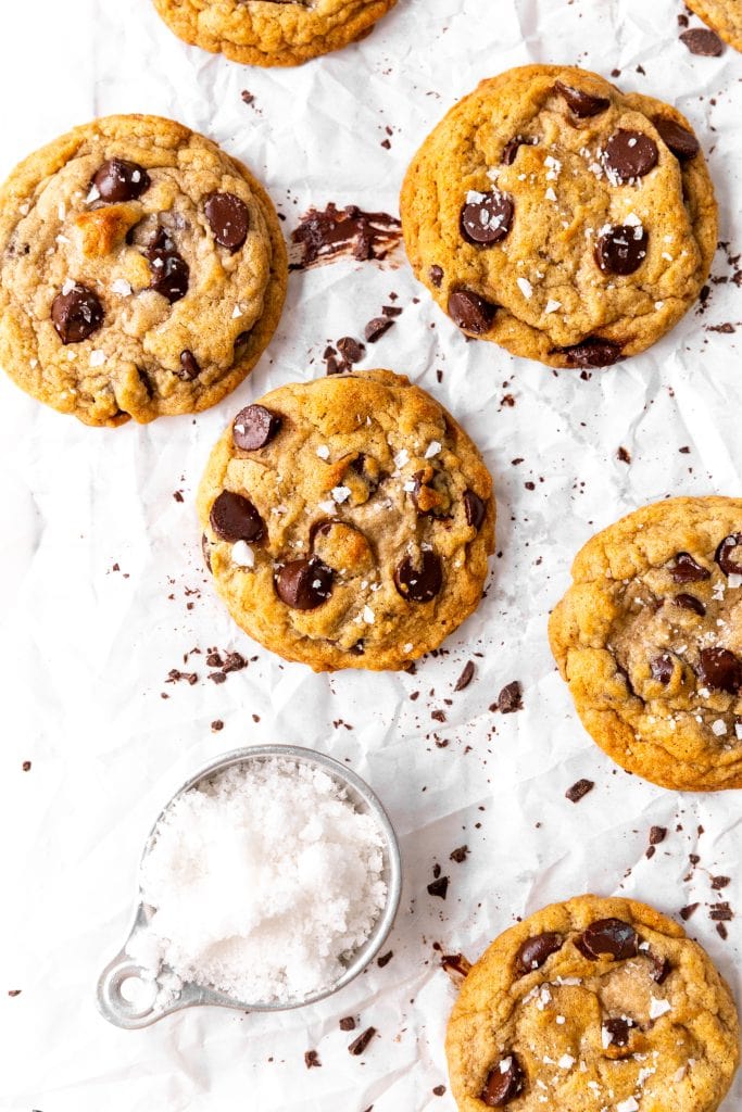 Banana chocolate chip cookies on a sheet of parchment with a cup of flaky salt.