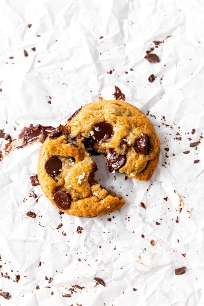 Vegan banana chocolate chip cookie broken in half on parchment paper.