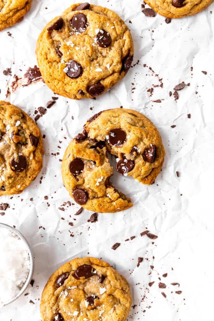 Banana chocolate chip cookies on parchment paper and a cup of flaky salt.